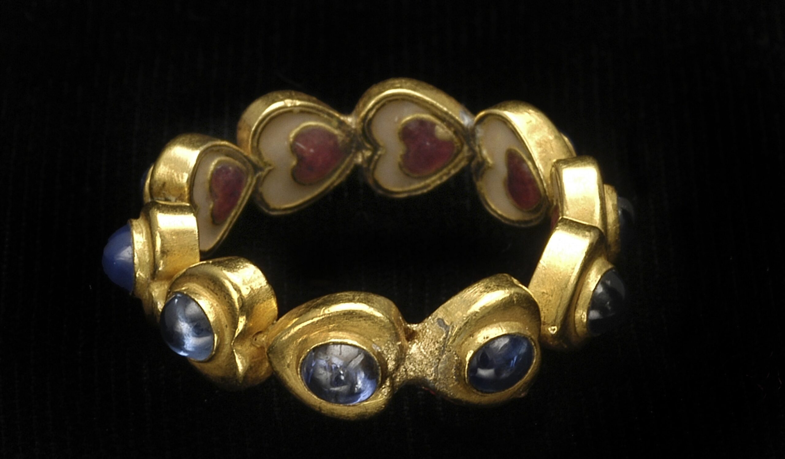 Antique gold ring with heart-shaped enamel segments and cabochon sapphires on black background