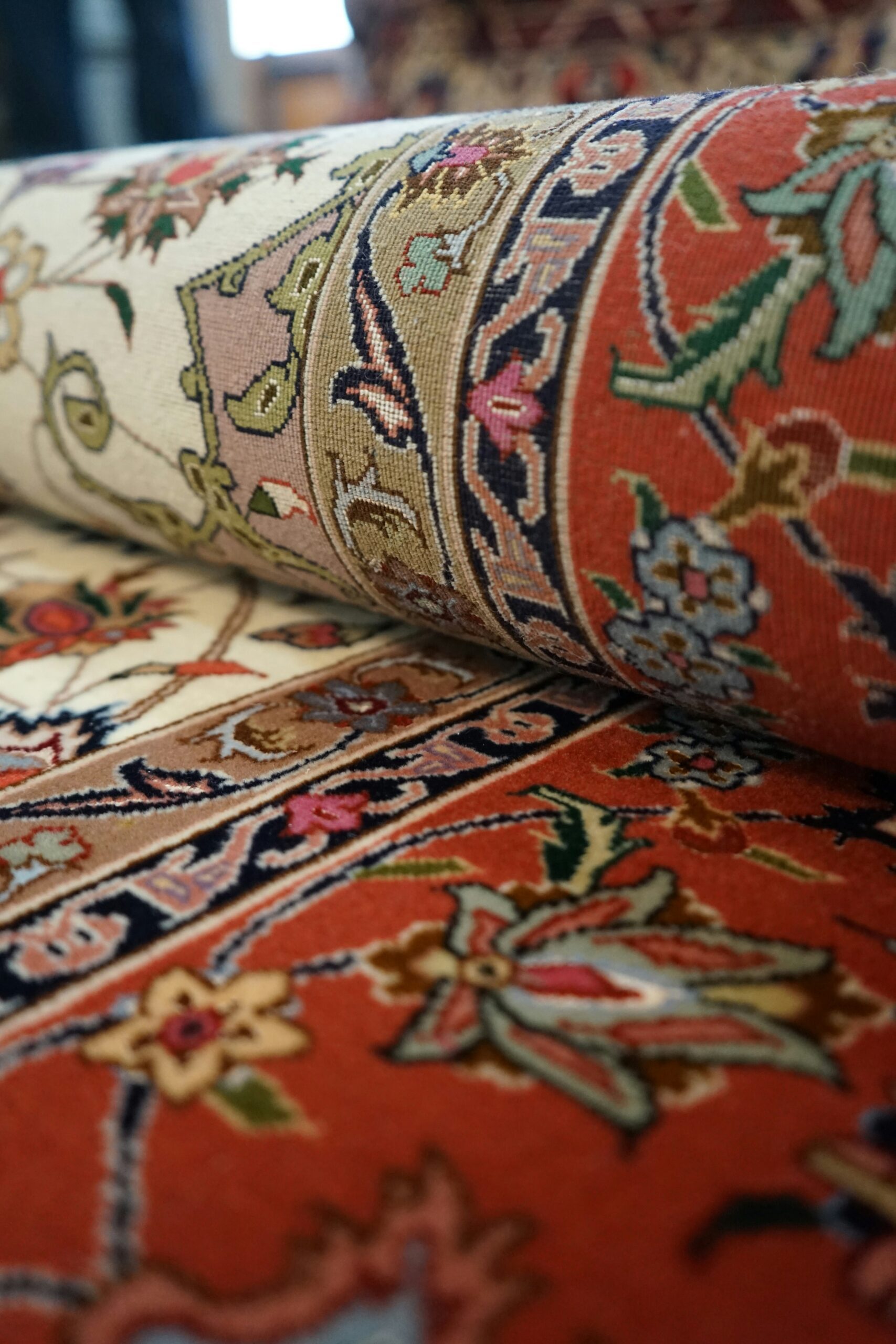Hand-knotted Persian carpet rolled to show intricate floral border patterns and dense pile in coral and navy