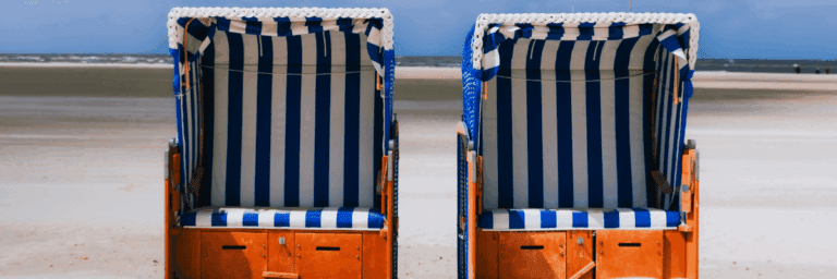 Two strandkorb wicker beach chairs with blue and white striped canopy on sandy German Baltic coast