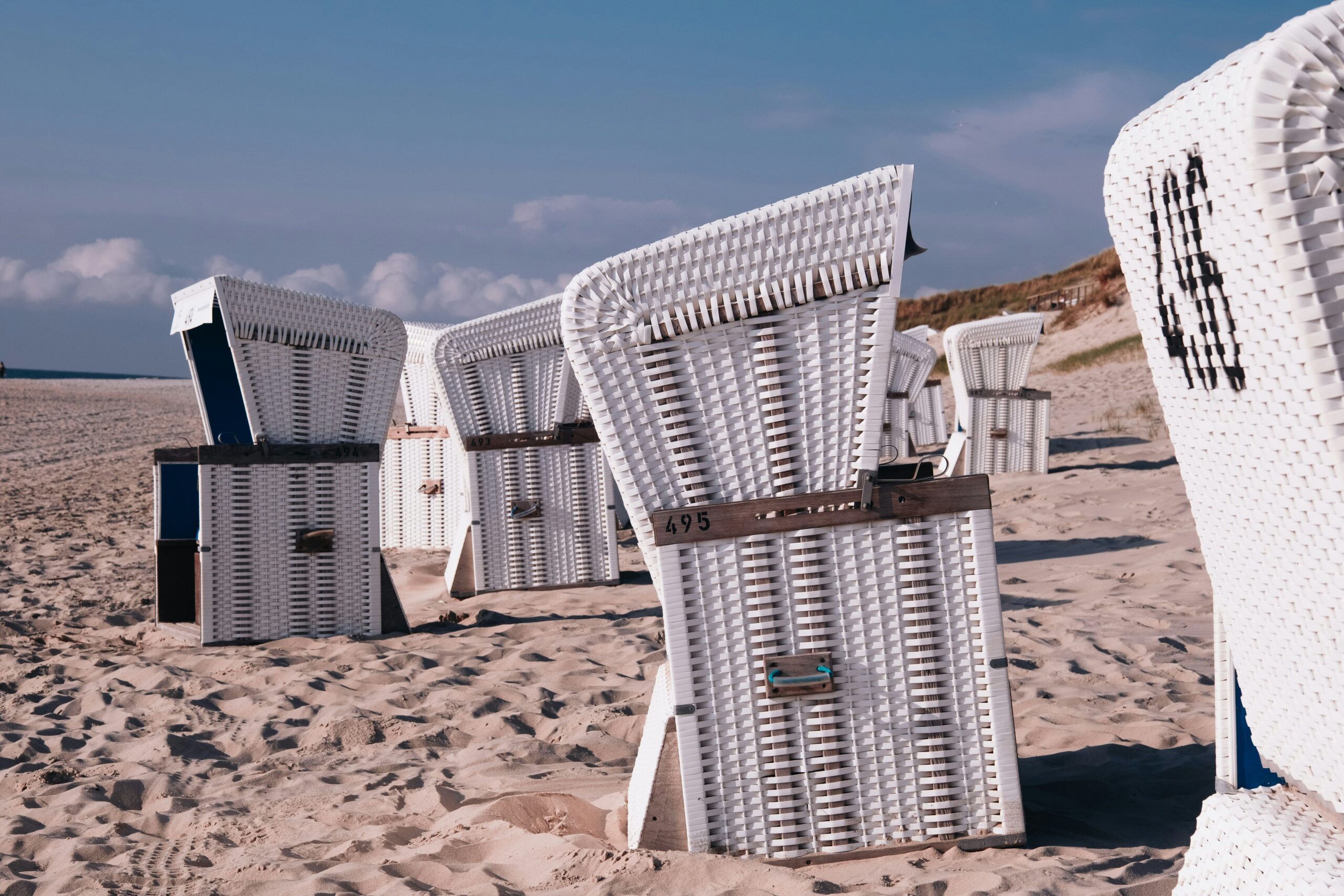 Strandkorb white wicker chairs with blue hoods on sandy dune overlooking North Sea.
