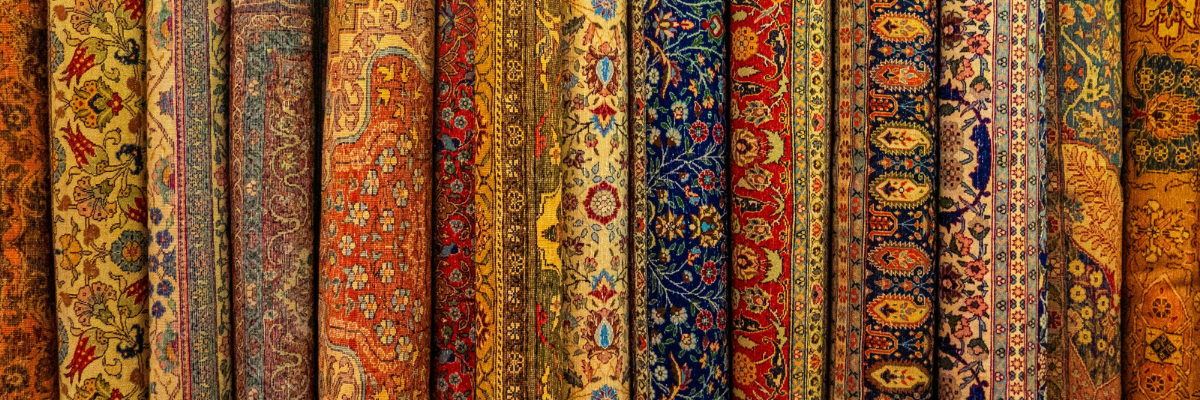 Stack of authentic hand-knotted Persian carpets showing intricate floral and geometric patterns in traditional colors at antique dealer