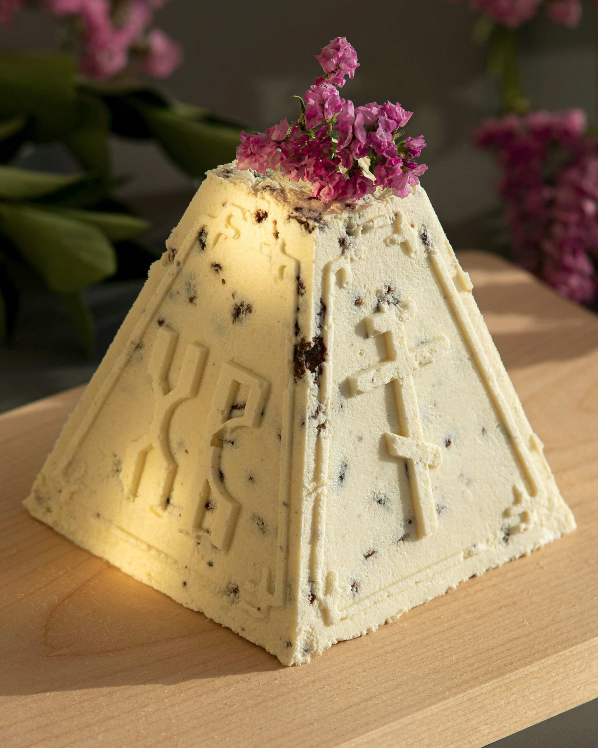 Russian paskha dessert pyramid with Cyrillic symbols and cross, topped with fresh flowers for Easter