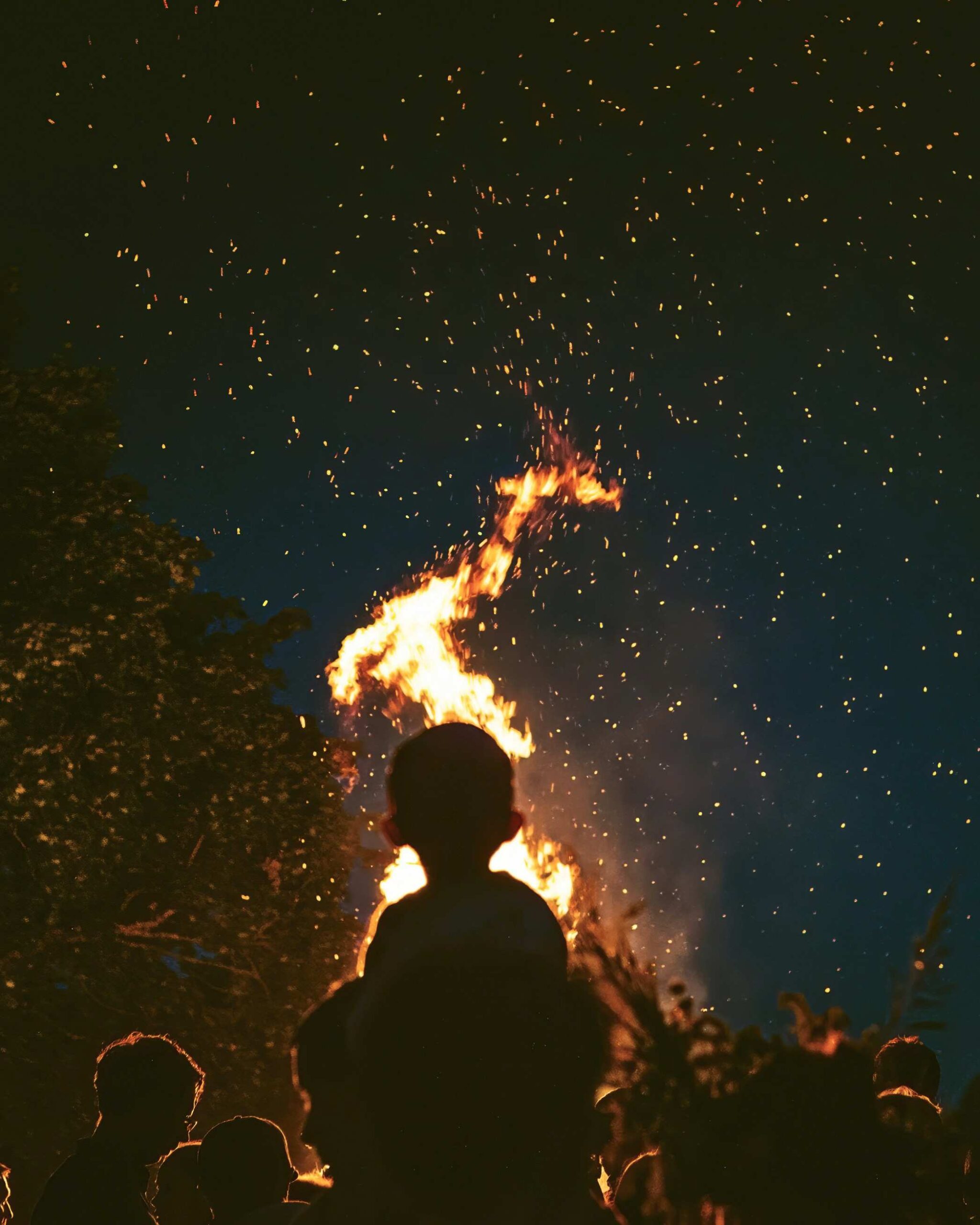 Silhouettes gathered around a blazing Easter bonfire at night — the ancient fire tradition of Holy Saturday