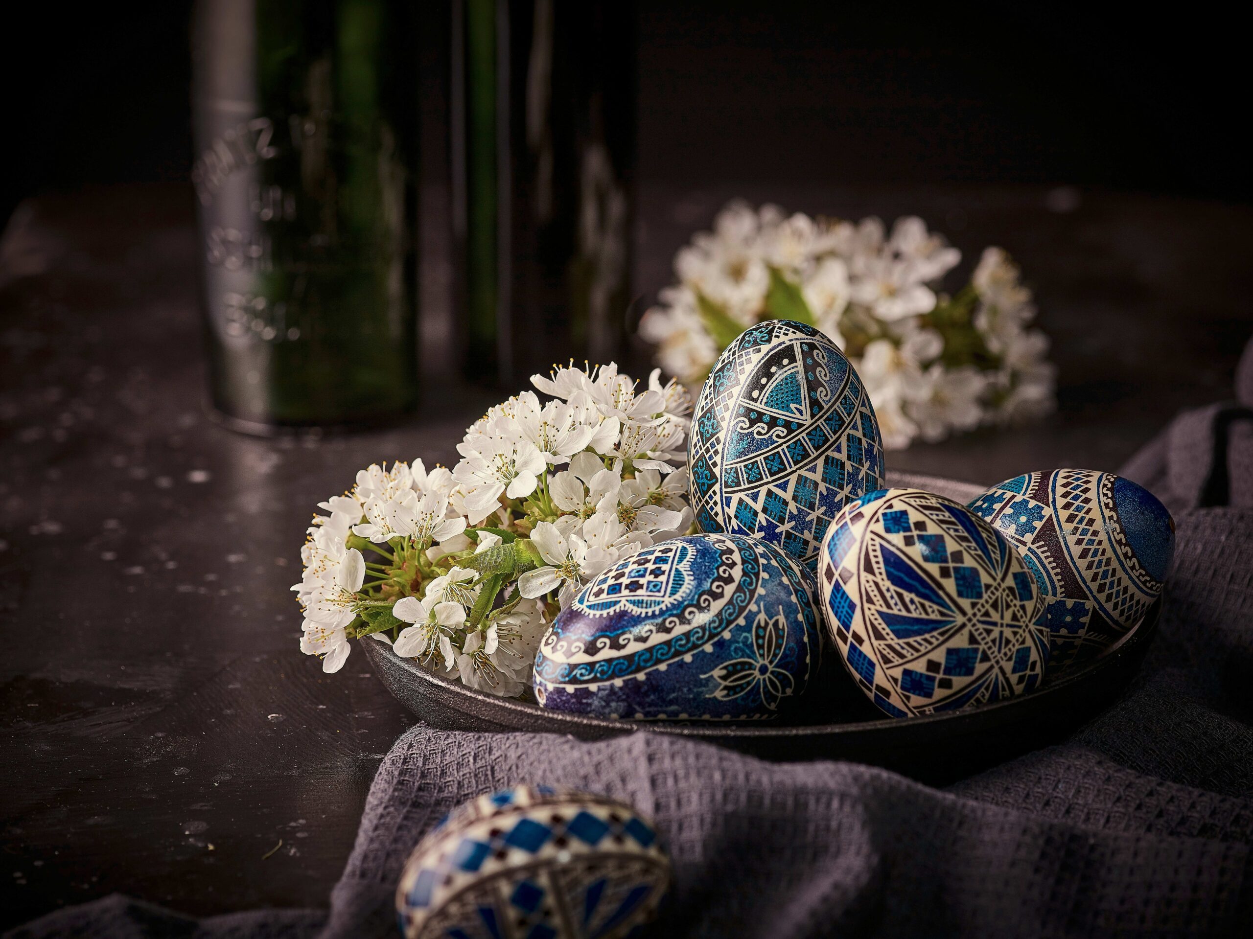 Romanian pysanka Easter eggs with intricate blue geometric patterns beside white spring blossoms